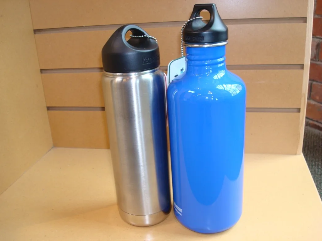 Twee roestvrijstalen drinkflessen, één zilverkleurig en één blauw, naast elkaar op een plank